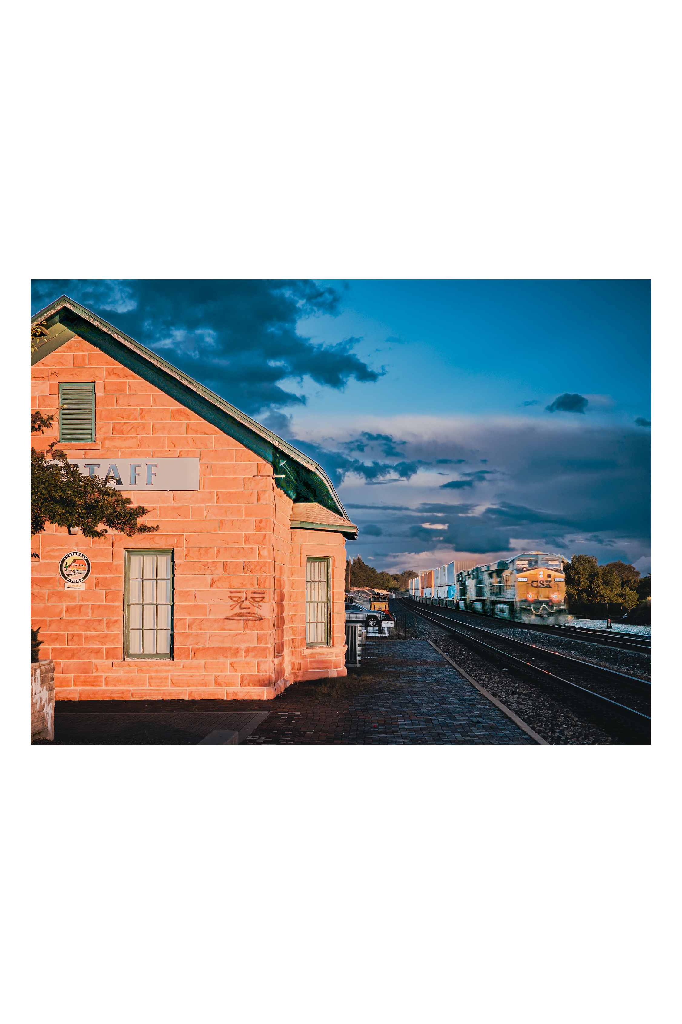 Flagstaff historic depot with freight train motion-blurred past under a storm sky