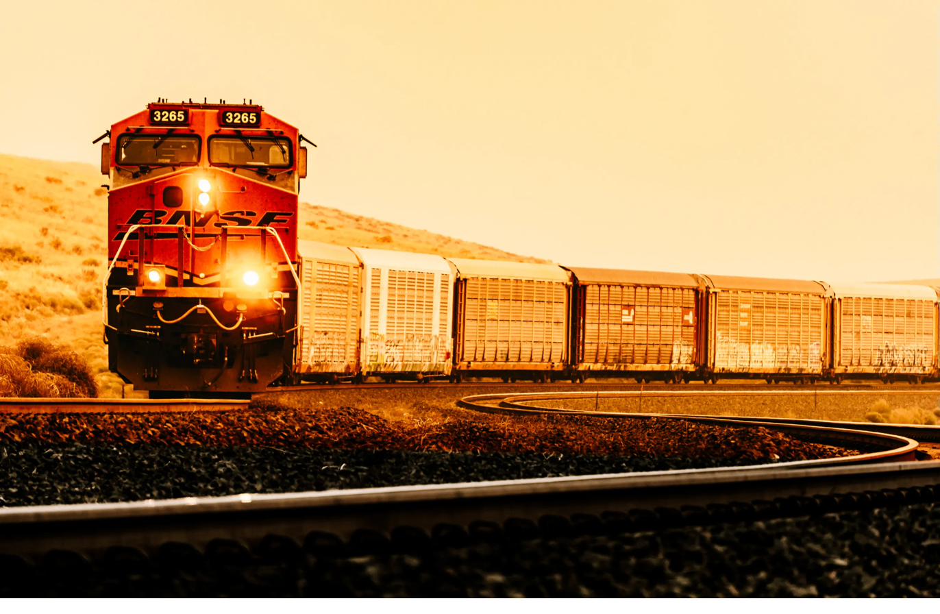 BNSF 3265 face-on in warm sepia light, auto-rack cars trailing into the curve