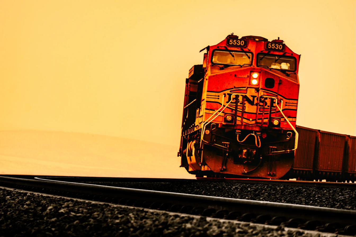 BNSF 5530 emerging from a golden horizon, ditch lights burning against the amber sky